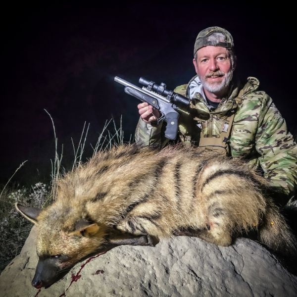 Jon Wayne Taylor at night with an aardwolf and a scoped Thompson Center Encore handgun