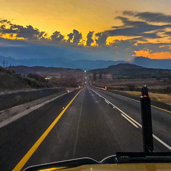 Empty highway running toward distant mountains under a burning orange dawn