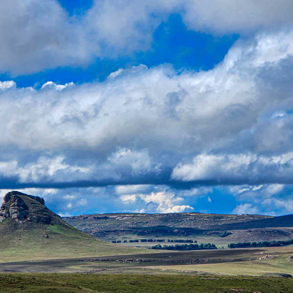 Rocky koppie rising from green plains under a broken cloud sky