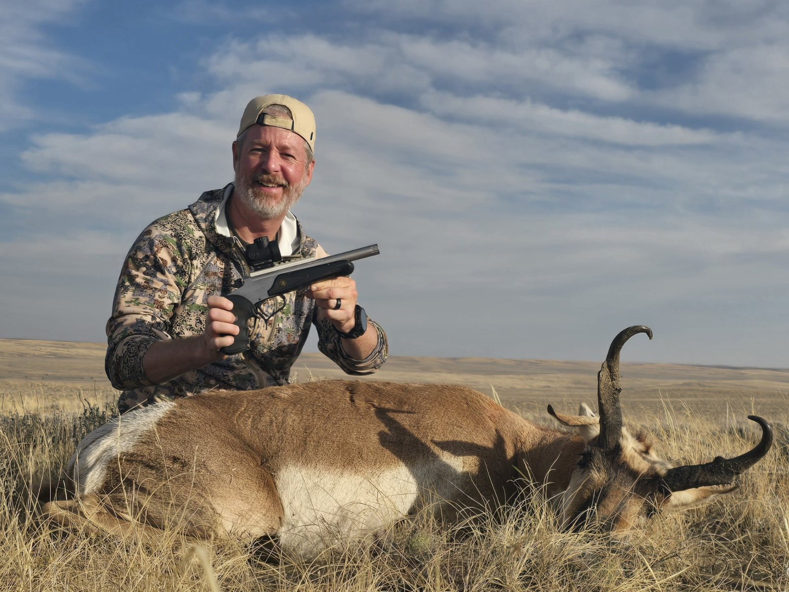 Jon Wayne Taylor with a pronghorn buck and a single-shot hunting handgun on open prairie